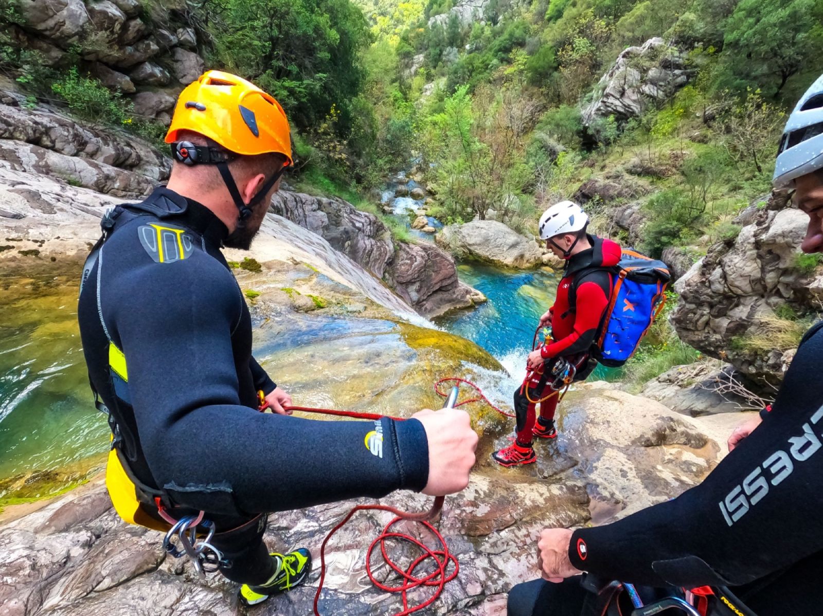 Guides in helmets and harnesses handling the rope at the top of a cascade